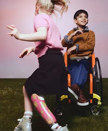 Boy in wheelchair plays with girl with lower limb prosthetic who wears high top trainers